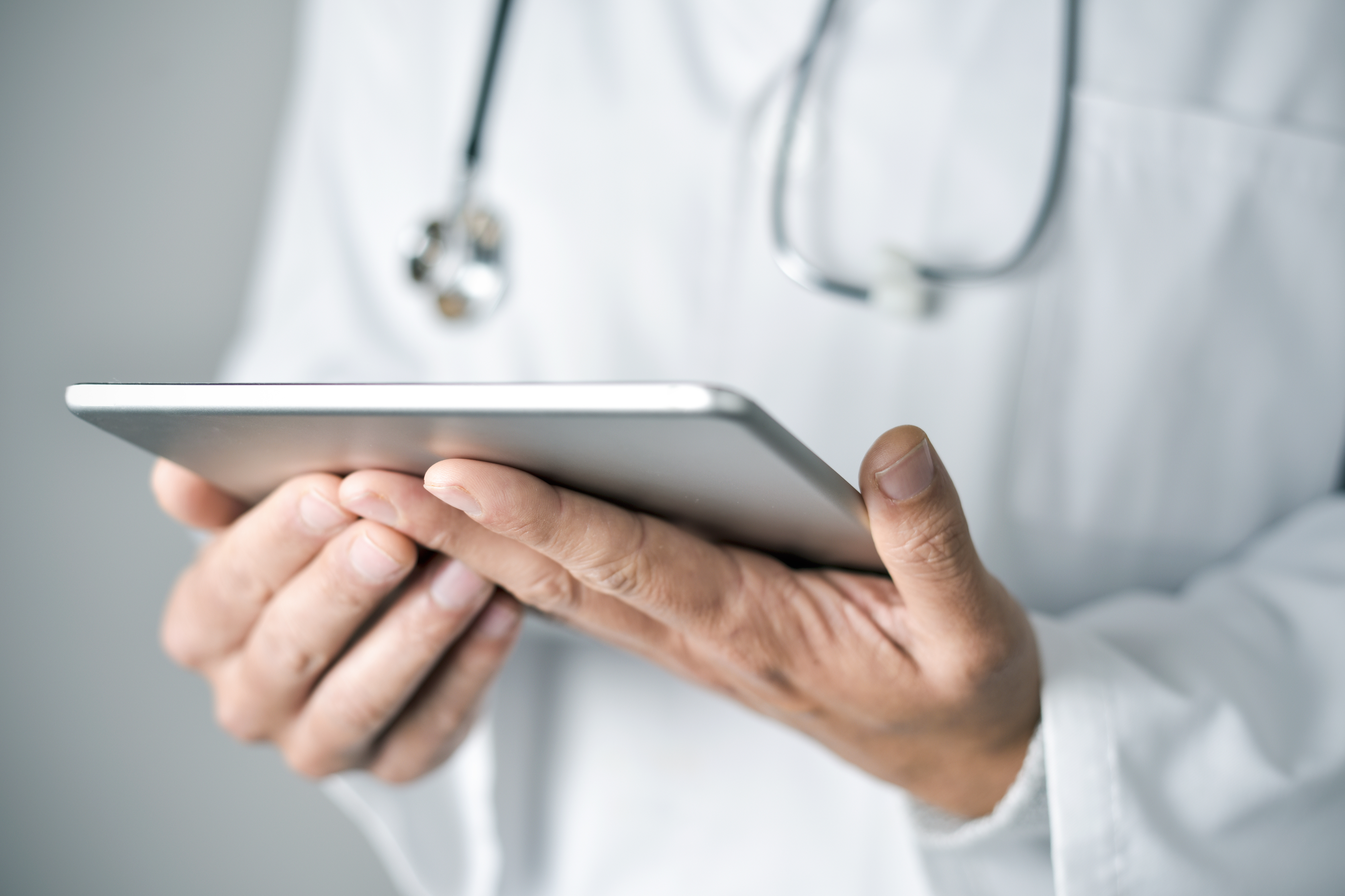 Lekarz w białym fartuchu trzyma w dłoniach tablet, a na szyi wisi mu stetoskop