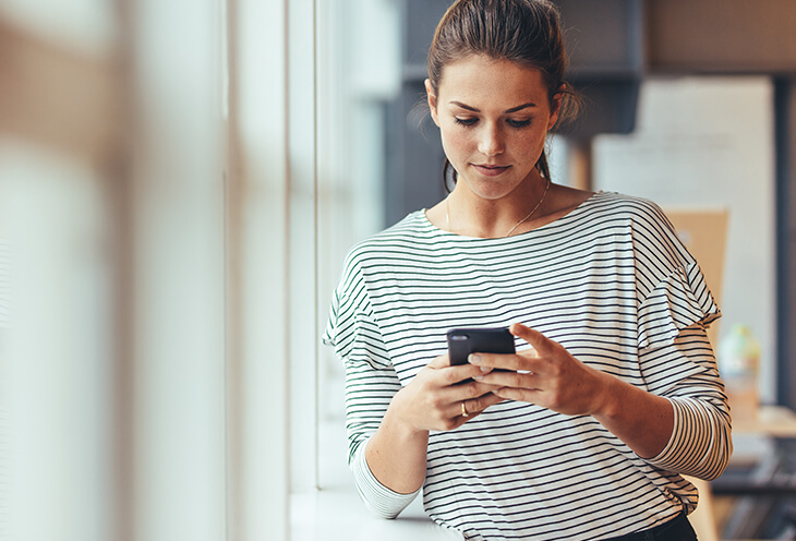 Młoda kobieta pisze wiadomość na telefonie. Zastanawia się, czy czasem nie cierpi na FOMO