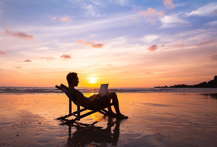 Programista siedzi na leżaku nad morzem przy zachodzie słońca i pracuje na laptopie