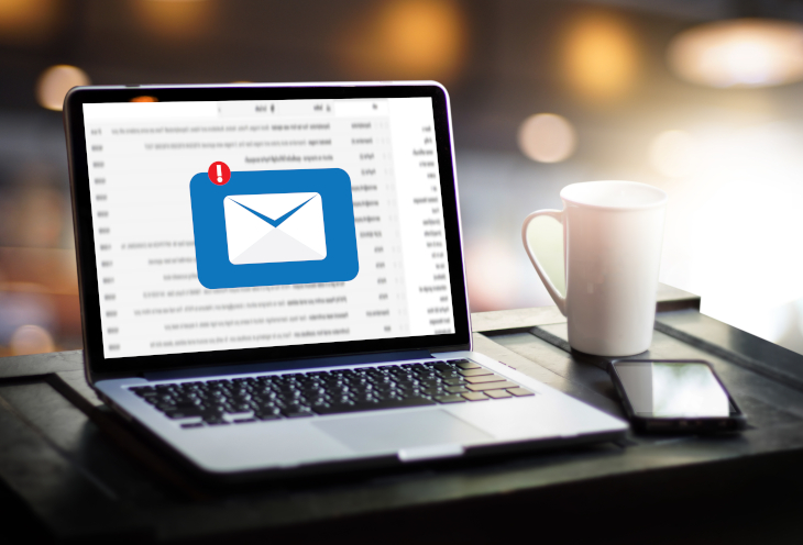 Na biurku stoi otwarty laptop, smartfon i kubek. Na ekranie widać nieodebraną wiadomość email