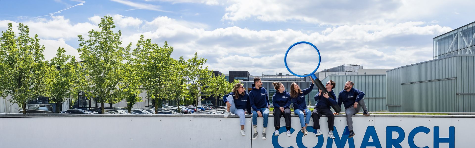 Zespół Employer Branding siedzący na murku z dużym logo Comarch