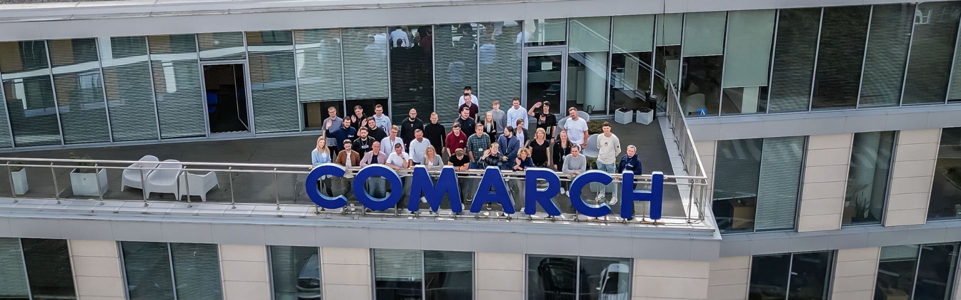 Widok z drona. Zespół pracowników Comarch pozuje do zdjęcia na tarasie biurowca w Lublinie. 