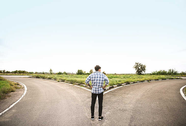 Młody mężczyzna stoi na rozstaju dróg. Ma do podjęcia ciężką decyzję 
