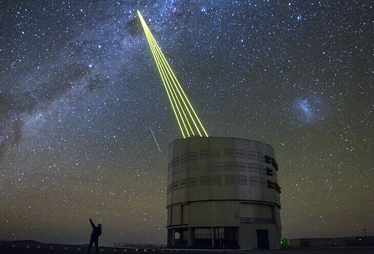 Wieża obserwacyjna na pustyni, która nocą łączy się z satelitą. Obok stoi mężczyzna z aparatem
