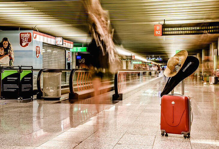 Czerwona walizka stojąca na dworcu kolejowym. Na rączce wisi paletka z logotypem Comarch 