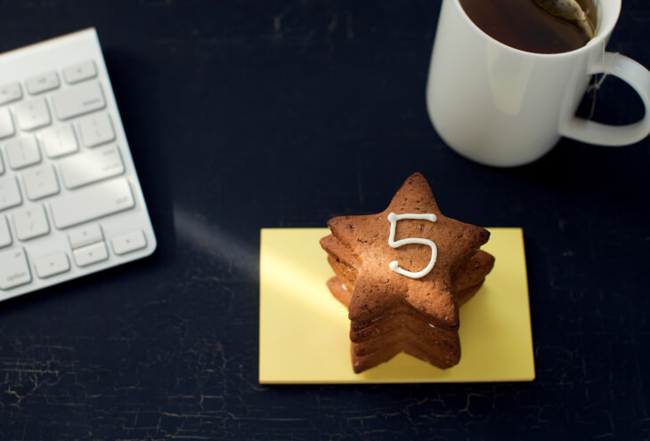 Na stole znajduje się klawiatura, kubek z kawą i ciastka w kształcie gwiazdki z numerem 5 na górze 