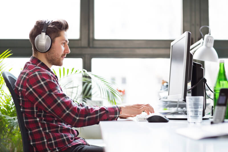 Młody mężczyzna w koszuli w kratę ze słuchawkami na uszach pracuje na komputerze
