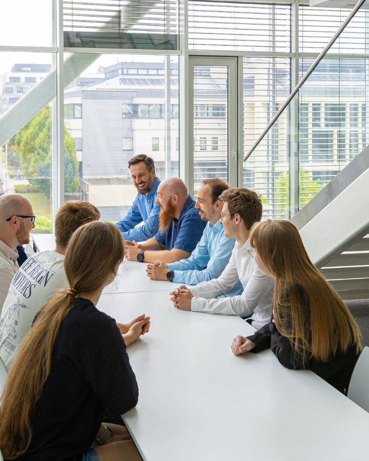 Zespół specjalistów ds. cyberbezpieczeństwa rozmawia przy dużym stole w przeszklonej przestrzeni budynku SSE6.