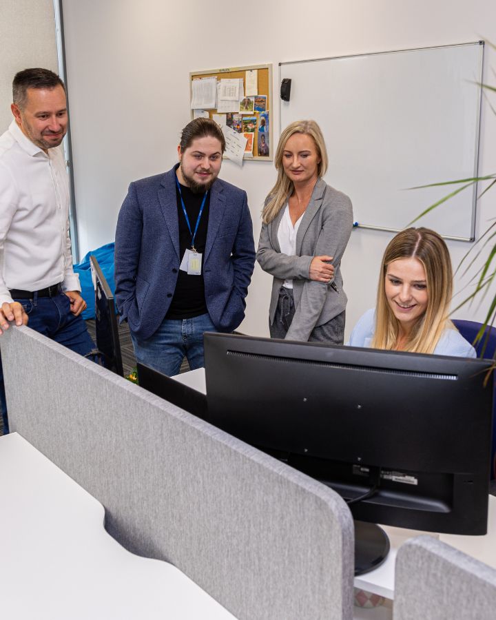 Kilkuosobowy zespół z uśmiechem dyskutuje przy biurku jednej z koleżanek.