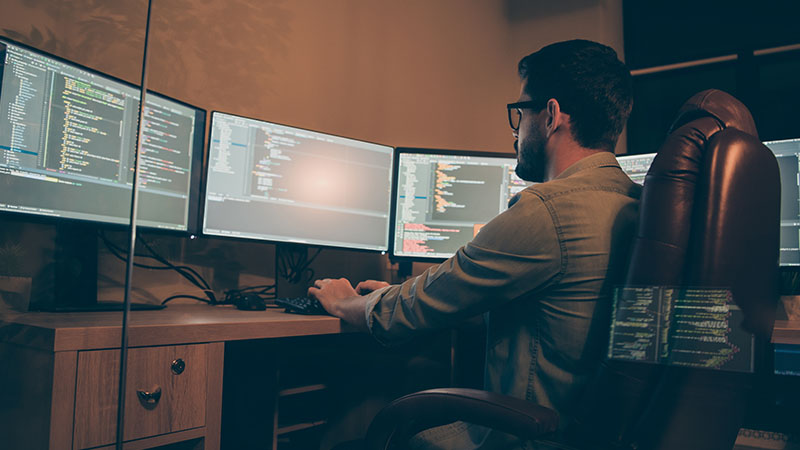Programista DevOps pracuje przy komputerze i dwóch monitorach.