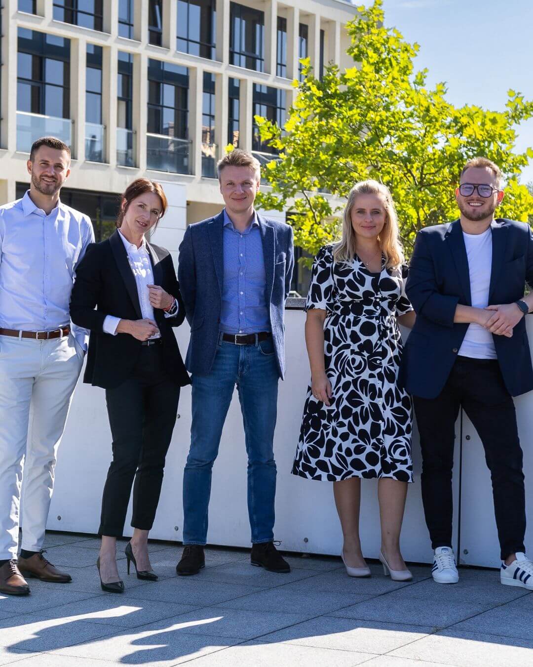 Zespół pracowników pozujących do zdjęcia na tle kampusu Comarch w Krakowie