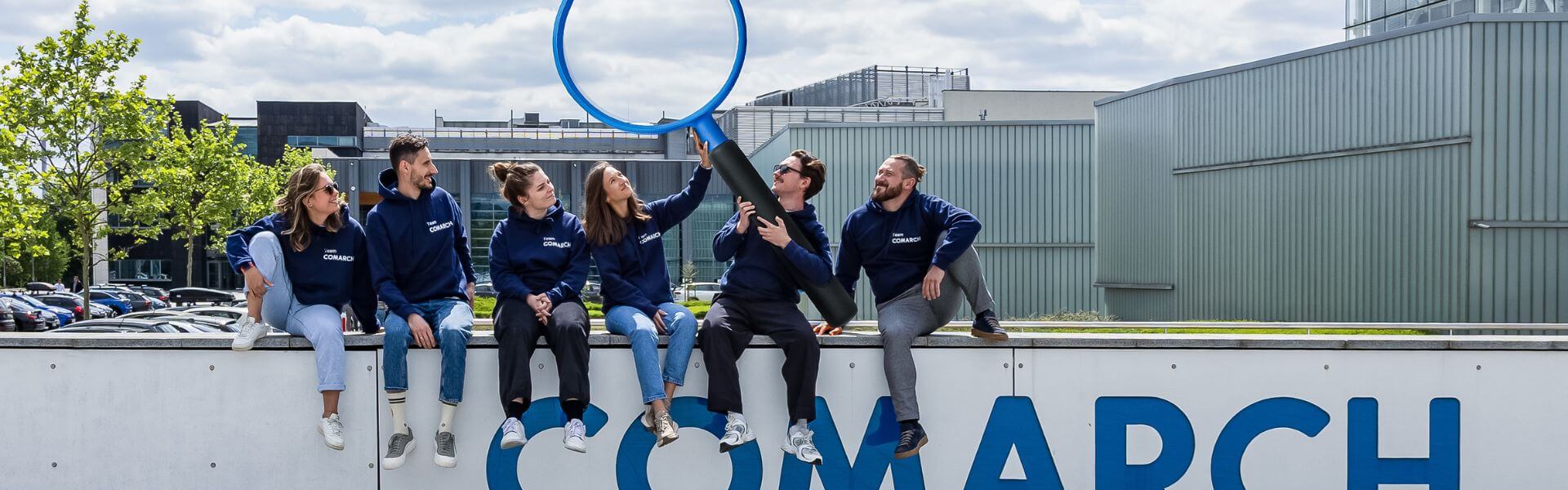 Zespół Employer Branding siedzący na terenie kampusu Comarch, trzymający wielką lupę