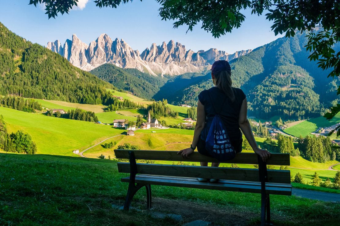 Kobieta siedząca na ławce z widokiem na górską panoramę. Na plecach plecak z logo Comarch.